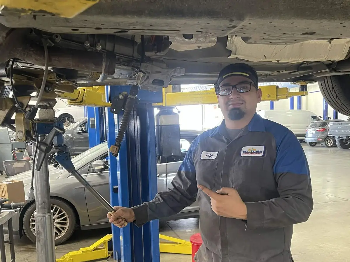Pablo working underneath a vehicle on a two-post lift with a torque wrench